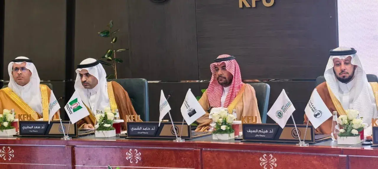 مجموعة وكلاء وممثلي الجامعات بزي رسمي يجلسون على طاولة اجتماع طويلة، أمام كل منهم لوحة تعريفية وأعلام صغيرة.